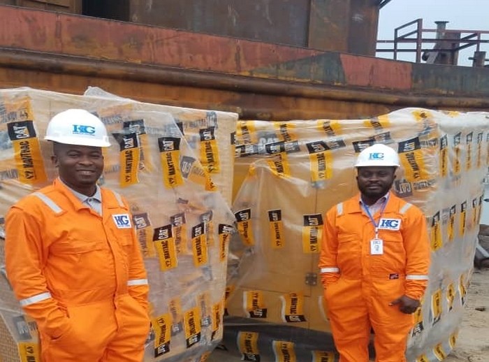 Two Kaizen Global staff in company coveralls and hard hats on duty beside palletised equipment